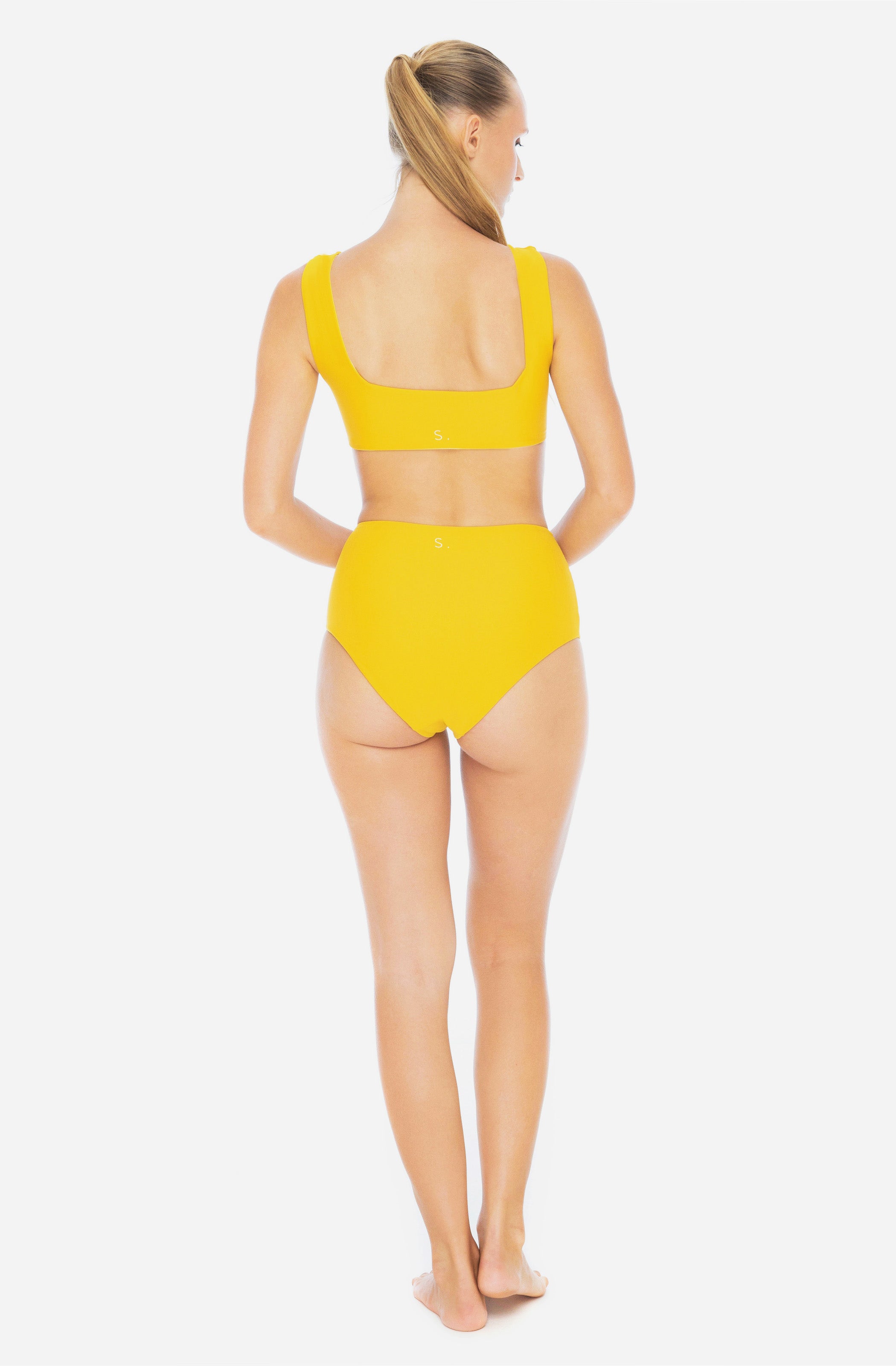 Back view of a woman modelling a surf bikini top and a high-waisted bikini bottom in saffron yellow.