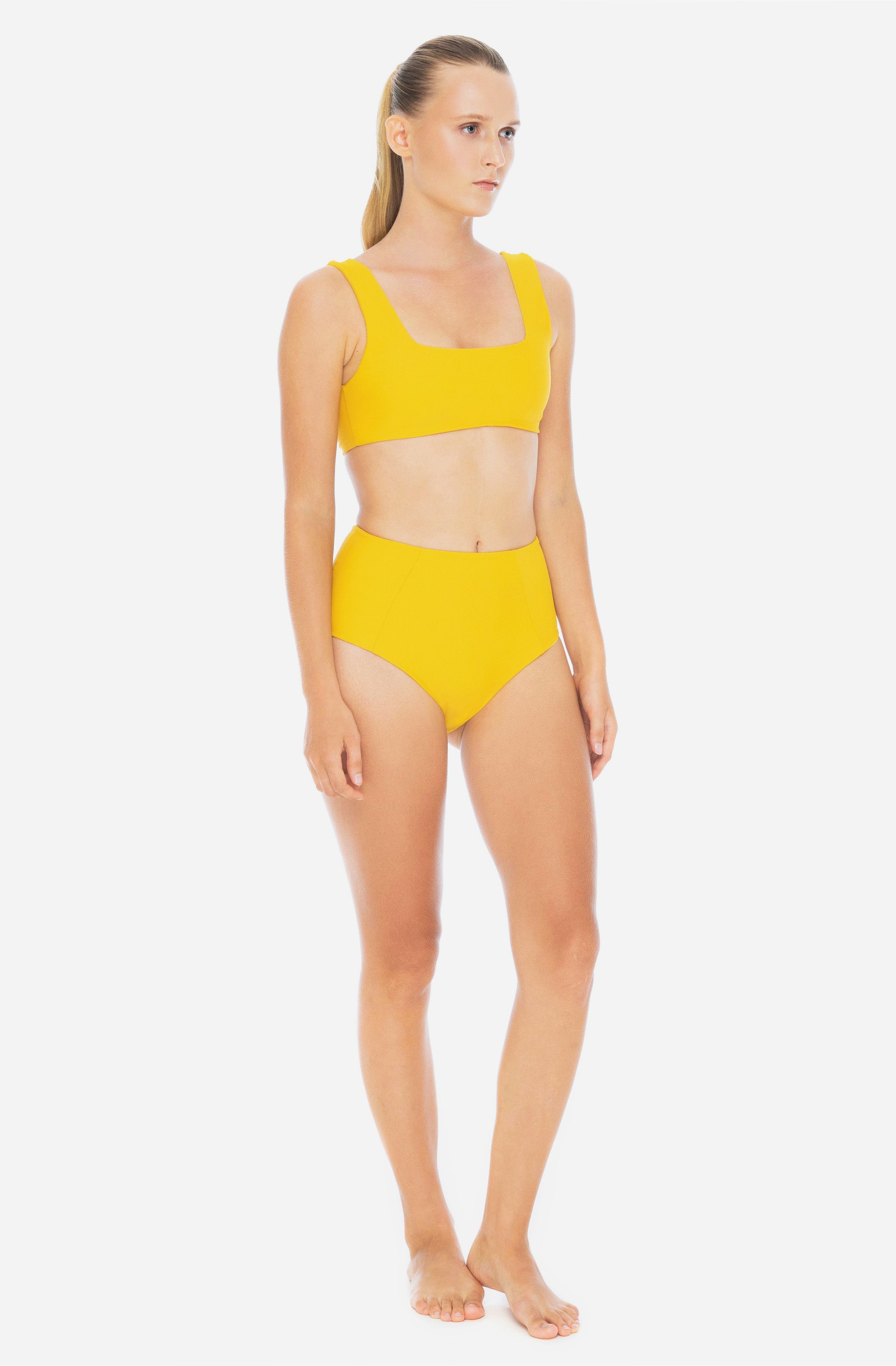 3/4 view of a woman modelling a surf bikini top and a high-waisted bikini bottom in saffron yellow.