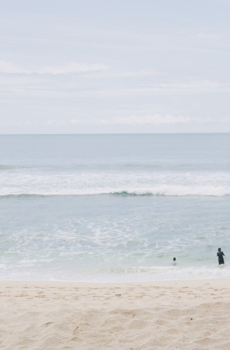 Woman standing in front of ocean wearing Surf_One_Piece_Lola_Black_Eco_Rib